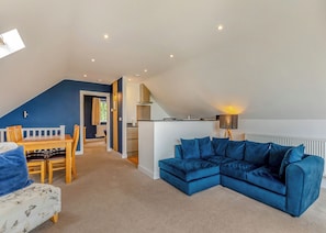 A loft-style living space with a dining area, a blue sectional sofa, a kitchen, and a staircase.