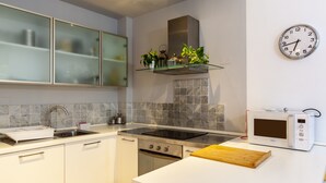 Une cuisine moderne équipée d’une cuisinière en acier inoxydable, d’un four à micro-ondes, d’un évier et d’une étagère en verre où sont disposées des plantes.