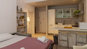 Une chambre d’hôtel de taille réduite, comprenant un lit, un petit bureau, une kitchenette et une salle de bain.