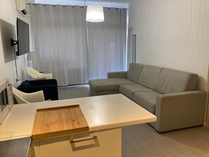 Un salon moderne avec un canapé, une table d’appoint en bois, un téléviseur et un luminaire au plafond.