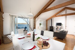 Un comedor con una mesa dispuesta para cuatro personas, chimenea, sofá y estantería.