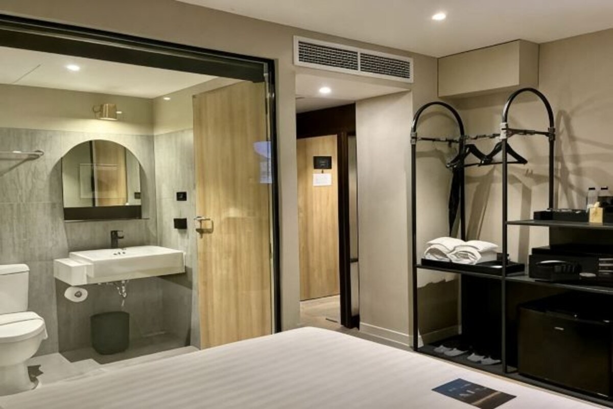 Un baño moderno con inodoro, lavamanos y ducha. Cuenta con una mampara de cristal y un perchero negro.