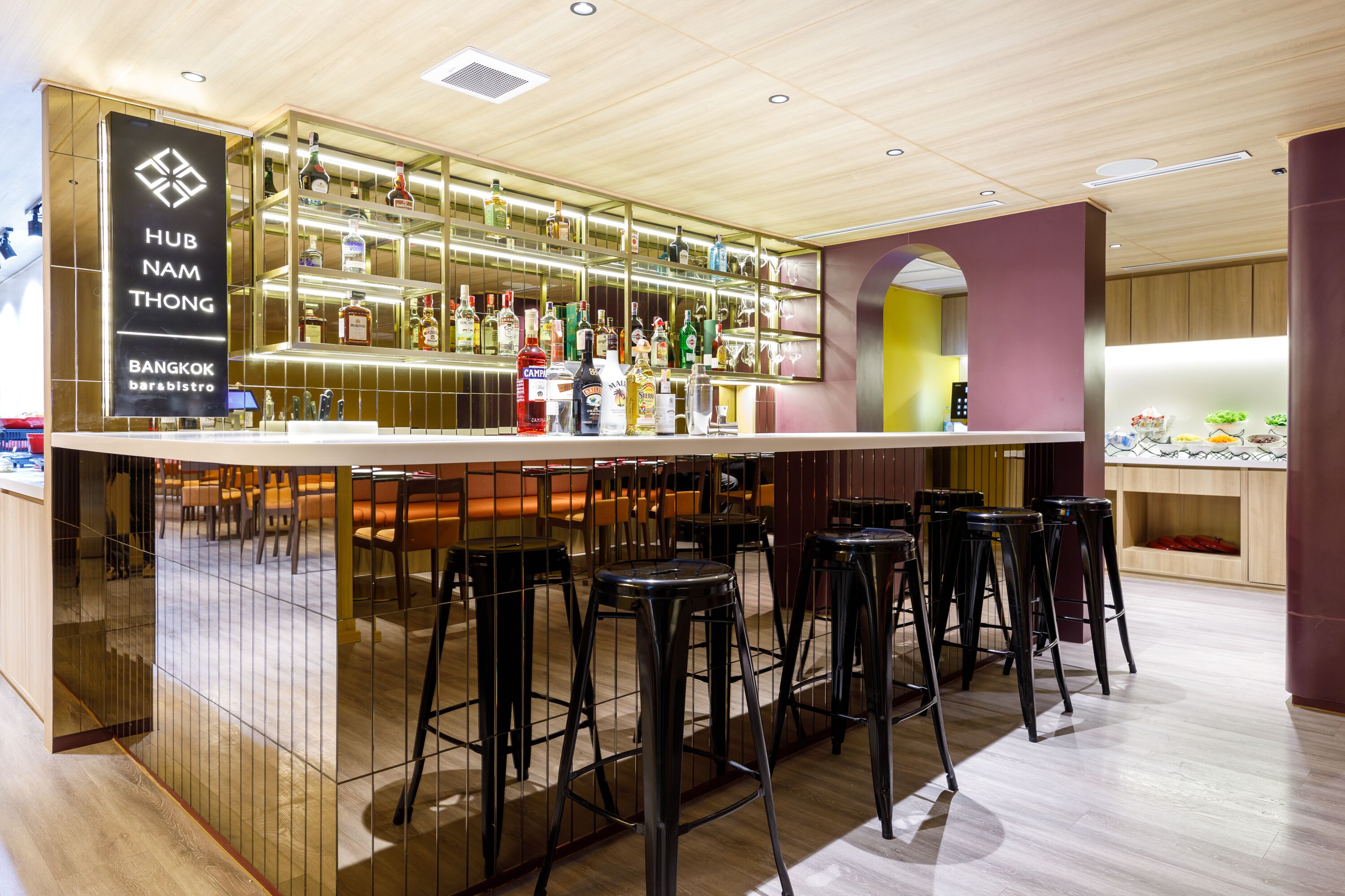 A bar area with stools, a bar counter, and shelves of liquor bottles.