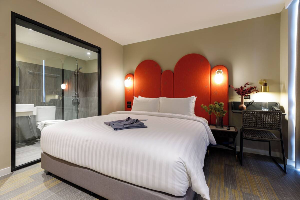 Een hotelkamer met een groot bed, een glazen douchecabine, een nachtkastje met een lamp en een stoel.