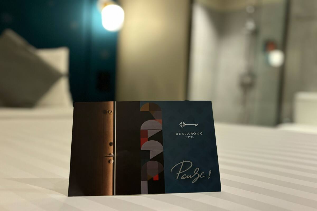 Een brochure van Benjalong Hotel op een bed met een gestreept dekbed.