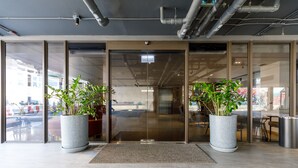 Uma entrada moderna com portas de vidro, duas grandes plantas em vasos e um chão de azulejos limpo.