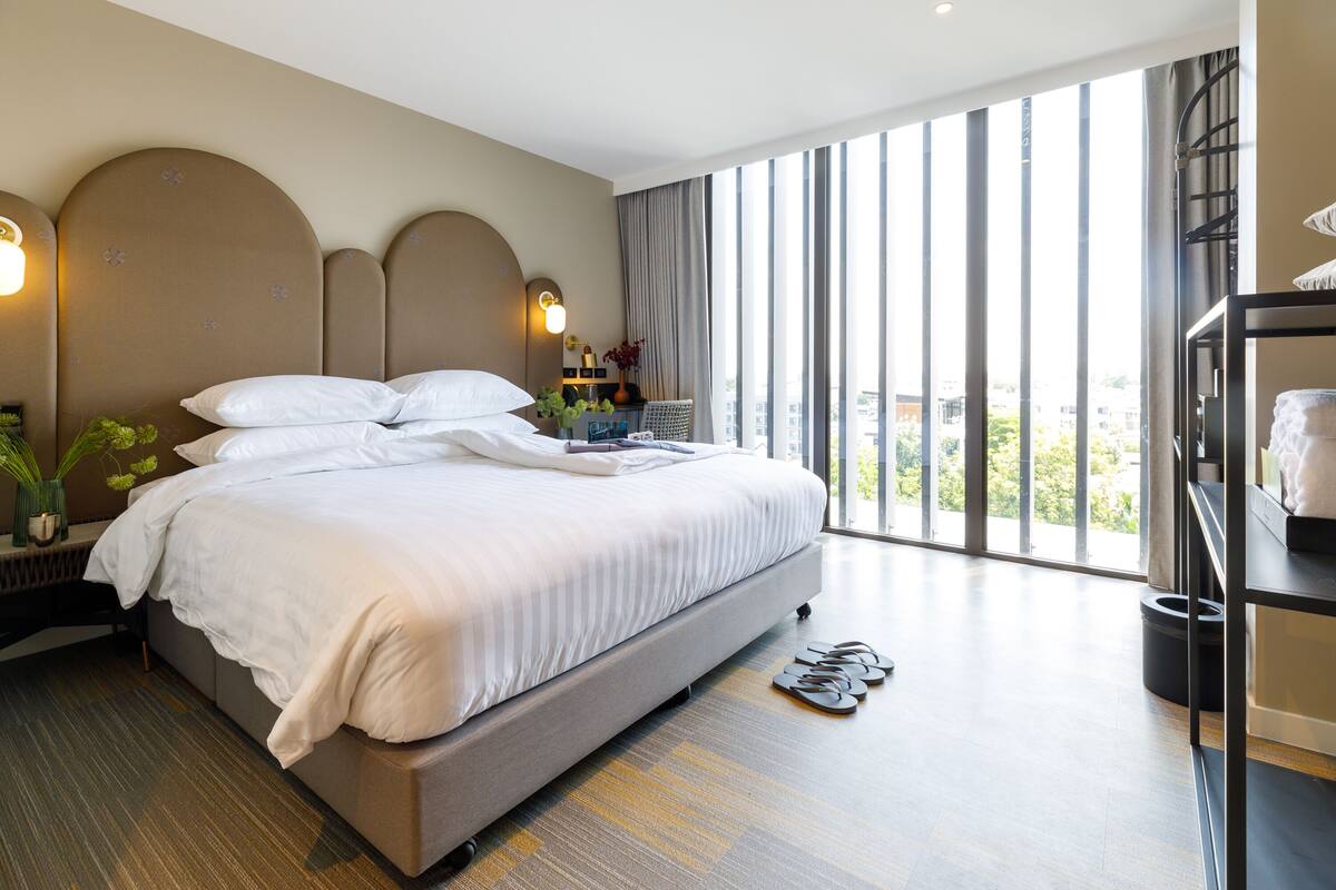 Een moderne hotelkamer met een groot bed, een bureau en uitzicht op de stad door grote ramen.