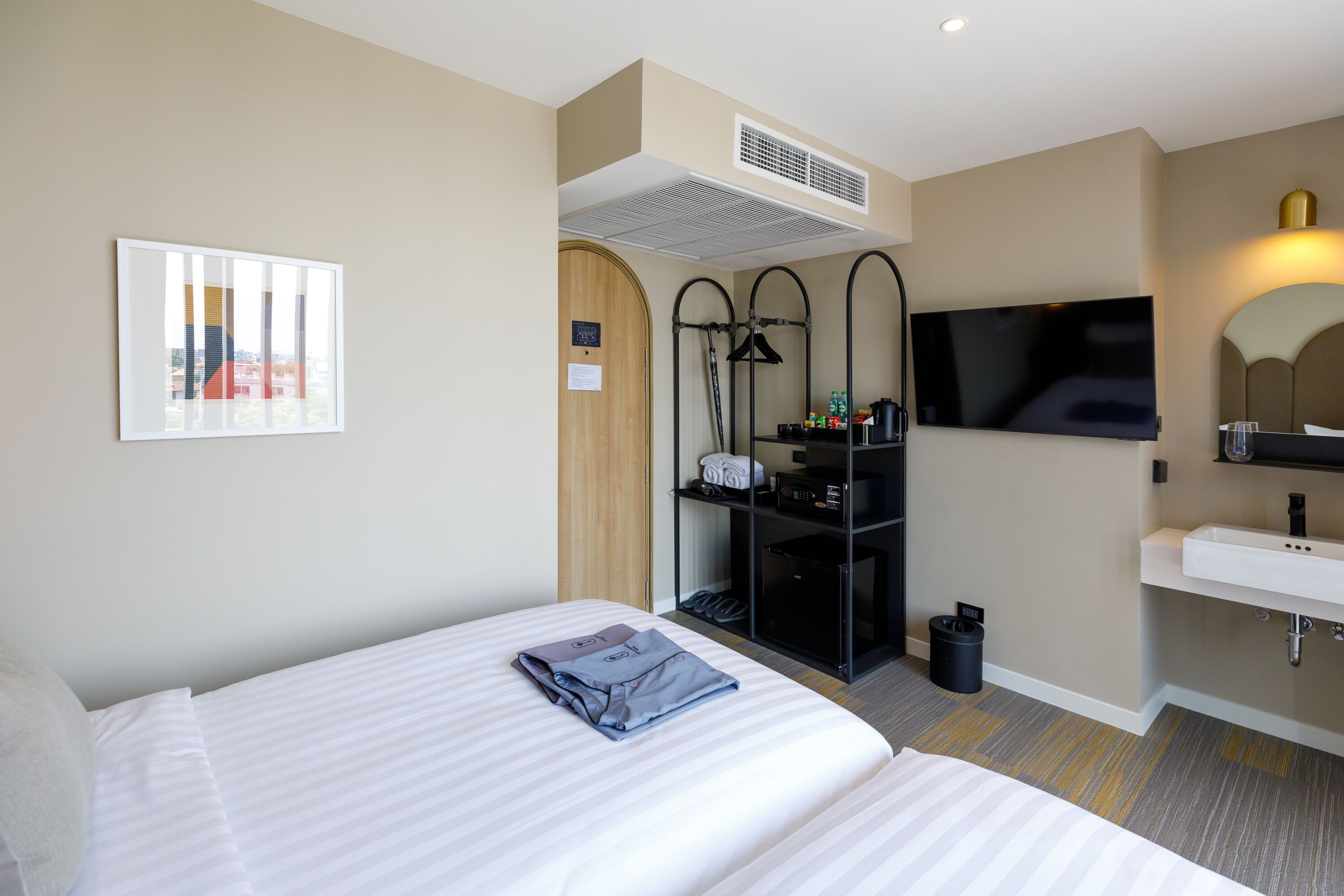 Habitación de hotel con dos camas, televisión, lavamanos y espejo.