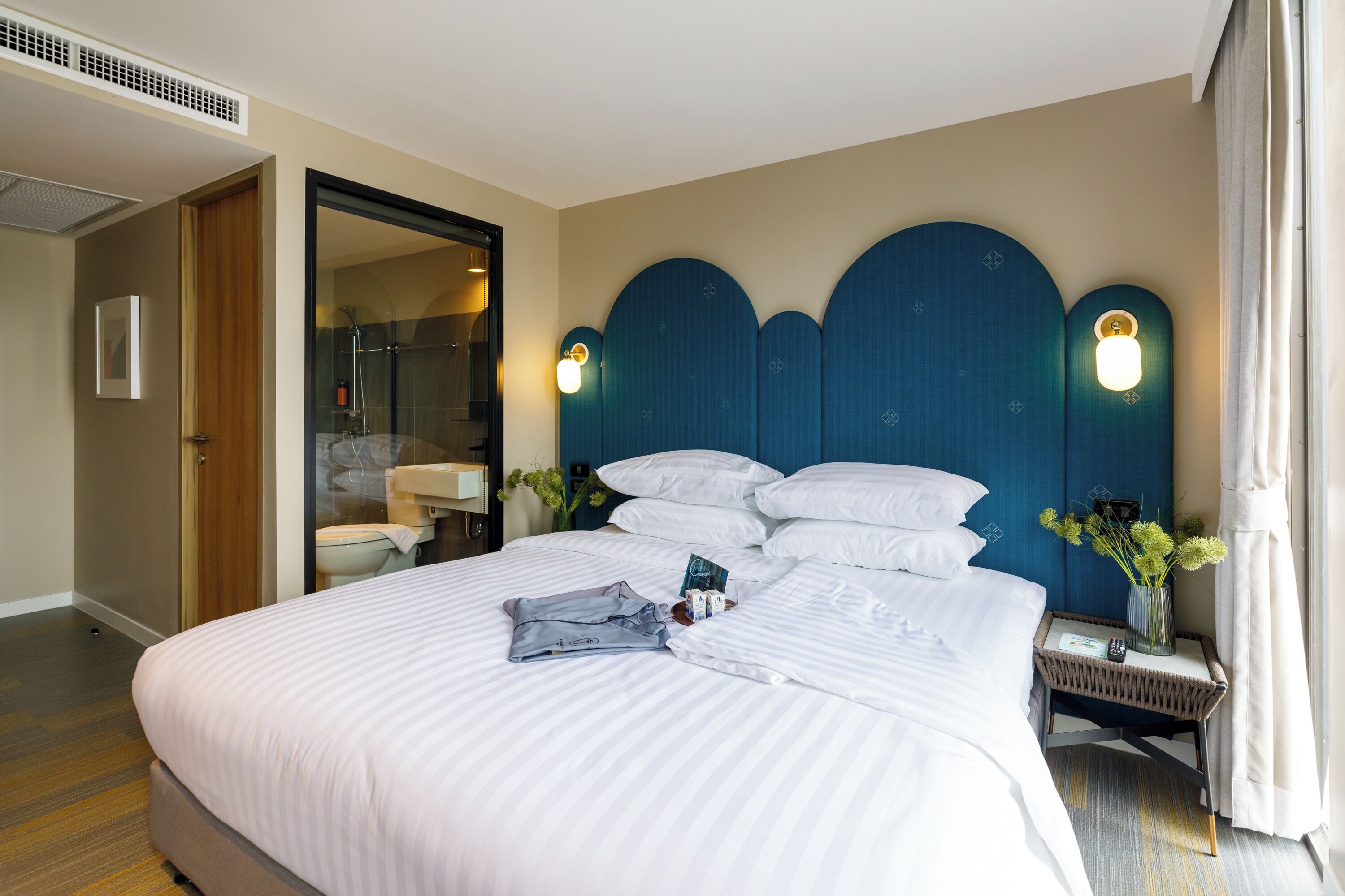 A hotel room with a large bed, a bedside table with a lamp, and a bathroom visible through an open door.
