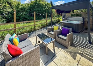 An outdoor patio area with wicker furniture, a hot tub, and a covered seating area.