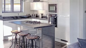 Une cuisine moderne dotée d’un îlot central, de tabourets de bar, d’une cuisinière à gaz, d’un four à micro-ondes et d’un réfrigérateur.