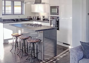 A modern kitchen with a central island, bar stools, a gas stove, a microwave, and a refrigerator.