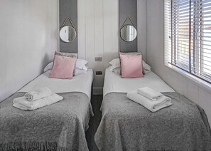 A hotel room with two beds, each with a pillow, a mirror, and a window with blinds.