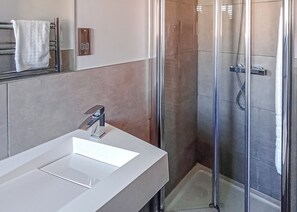 A modern bathroom with a white sink, a glass shower enclosure, and a towel hanging on a rack.