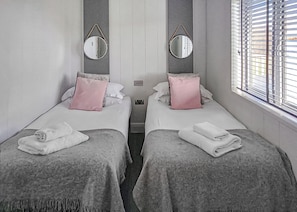 A hotel room with two beds, each with a pillow, a mirror, and a window with blinds. - 3 bedroom accommodation in Newbury (Newbury)