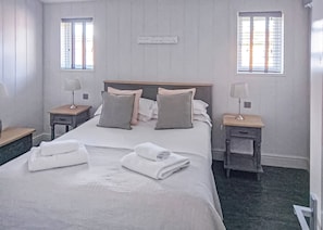 A neatly made bed with pillows and towels, two bedside tables with lamps, and two windows with blinds.