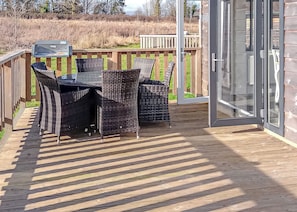 Un patio al aire libre con una mesa, sillas, una parrilla y una terraza de madera.
