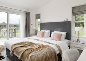 A bedroom with a large bed, a nightstand, a lamp, and a view of the outdoors.