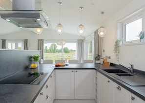 A modern kitchen with a central island, built-in appliances, pendant lighting, and a view of the outdoors.