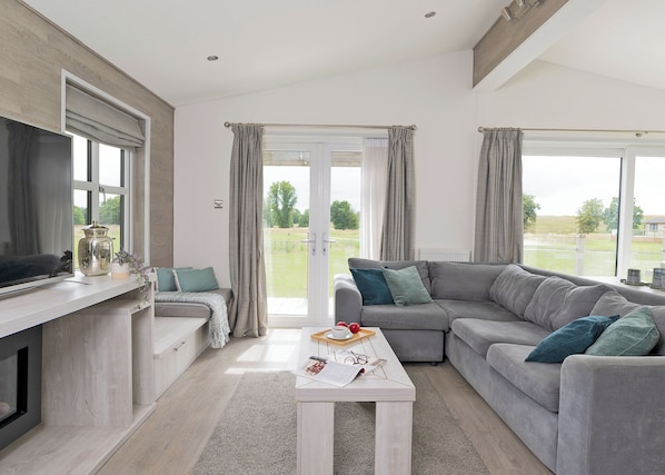 A modern living room with a sofa, a coffee table, a TV, and a view of the outdoors.
