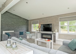 A modern living room with a fireplace, grey sofas, a flat-screen TV, and large windows.