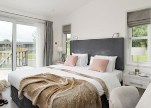 A bedroom with a large bed, a nightstand, a lamp, and a view of the outdoors.