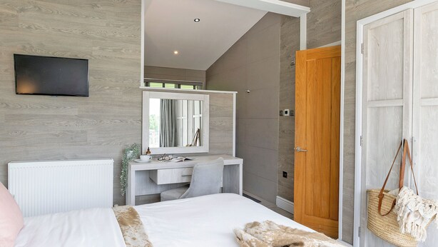 A bedroom with a bed, a bedside table, a mirror, a dresser, a TV, and a door.