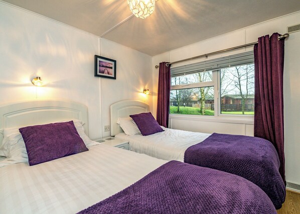 A hotel room with two beds, a window with curtains, a picture on the wall, and a ceiling light fixture.