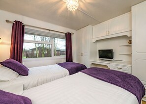 A bedroom with two beds, a television, and a window with curtains.