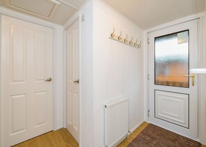 A hallway with white doors, a radiator, a coat rack, and a glass door with a view.