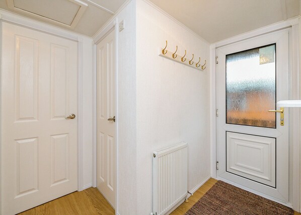 A hallway with white doors, a radiator, a coat rack, and a glass door with a view.