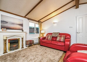 Uma sala de estar com lareira, um sofá de couro vermelho, um almofado xadrez e um quadro na parede.
