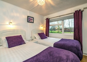 A hotel room with two beds, a window with curtains, a picture on the wall, and a ceiling light fixture.