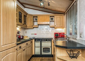 A kitchen with wooden cabinets, a stove, an oven, a microwave, and a window with blinds.