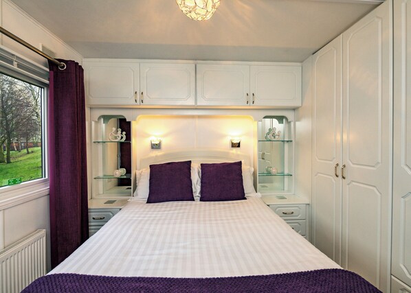 A bedroom with a bed, two nightstands, a dresser, and a window with curtains.