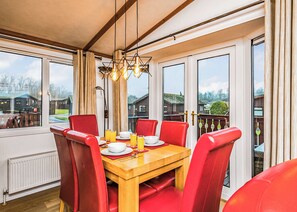 A dining area with a wooden table, red chairs, and a view of houses through large windows.