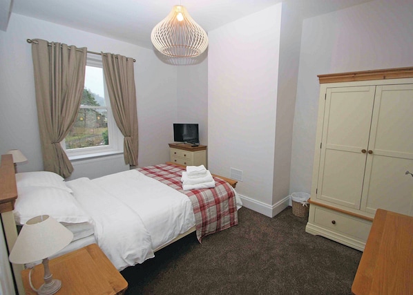 A bedroom with a bed, a television, a wardrobe, and a window with curtains.