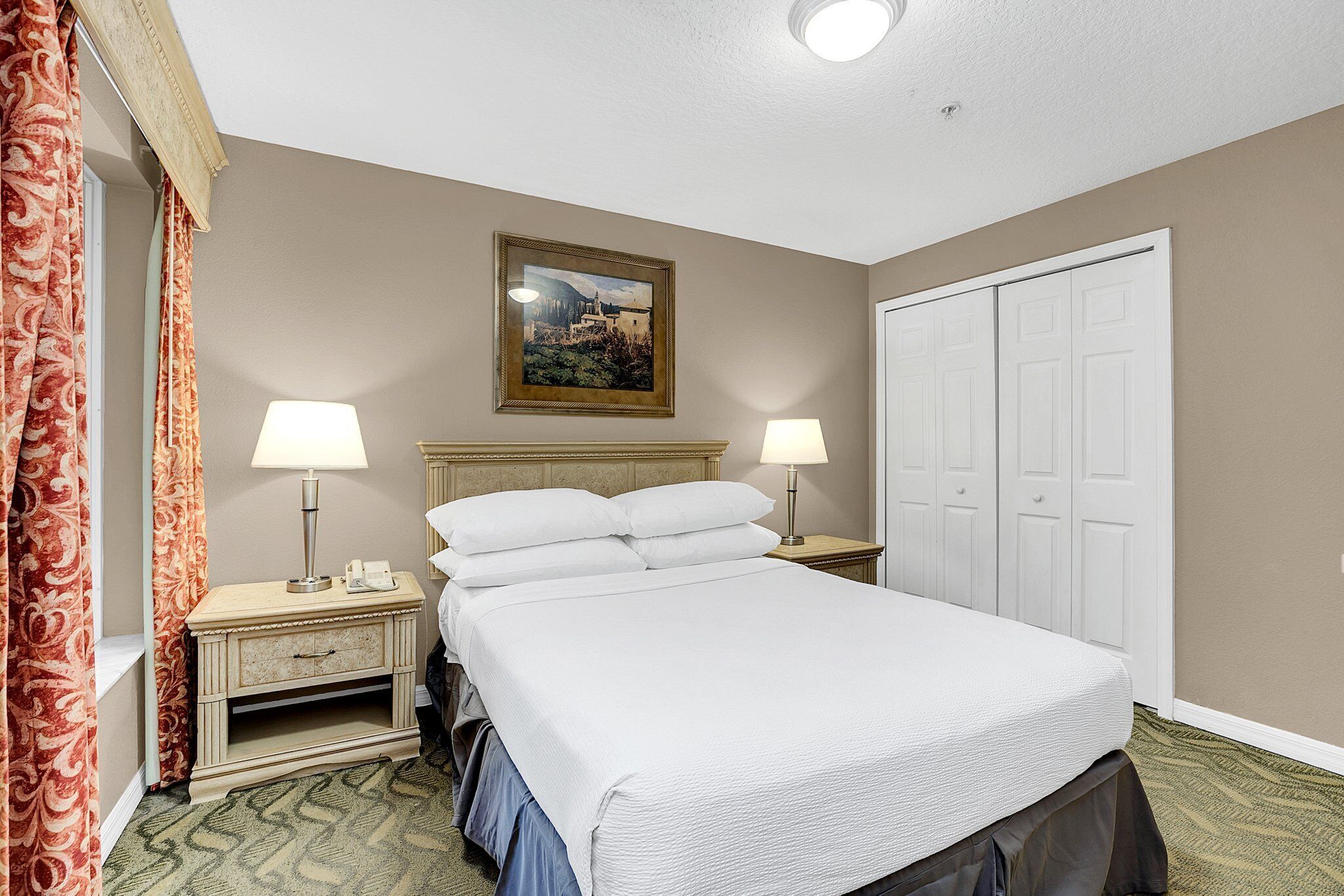 A hotel room with a bed, two bedside lamps, a nightstand, a dresser, a door, and a painting on the wall.