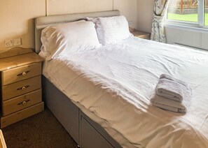 Un lit bien fait, avec du linge de lit blanc, une table de chevet en bois dotée de tiroirs et une fenêtre avec des rideaux.