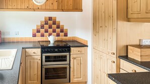 A kitchen with wooden cabinets, a black countertop, a stove, and an oven.