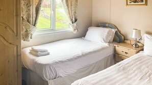 A bedroom with two beds, a window with curtains, a bedside table with a lamp, and a wardrobe.