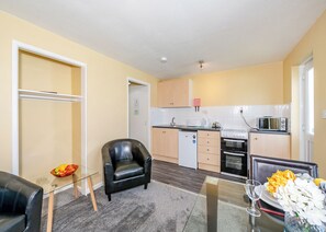Un espace de vie compact comprenant un coin cuisine, une table à manger en verre, un fauteuil en cuir et un petit réfrigérateur.