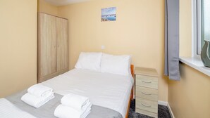 Een slaapkamer met een bed, een kledingkast, een raam met gordijnen en een schilderij aan de muur.