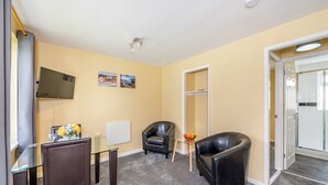 Hotelkamer met een glazen tafel, twee lederen fauteuils, een aan de muur bevestigde televisie en een deur naar een balkon.