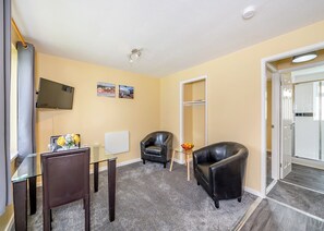 Une chambre d’hôtel avec une table en verre, deux fauteuils en cuir, un téléviseur fixé au mur et une porte donnant sur un balcon.