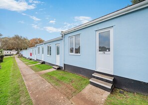 A row of light blue mobile homes with white doors and windows, numbered 78, with a paved path and grass in front.