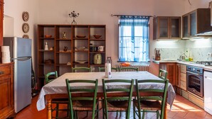 A kitchen with a dining table, chairs, a refrigerator, a stove, and a window with curtains. - Villa 'Podere Par di Rota' with Pool, Terrace and Wi-Fi (Calci)