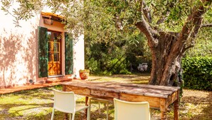 A wooden table with chairs in a garden setting, a building with a door and shutters, and a large tree. - Villa 'Podere Par di Rota' with Pool, Terrace and Wi-Fi (Calci)