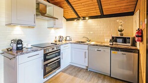 A modern kitchen with white cabinets, stainless steel appliances, a wooden ceiling, and a brick backsplash.