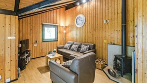 A cozy cabin interior with a wooden interior, a sofa, a small table, a television, and a wood-burning stove.